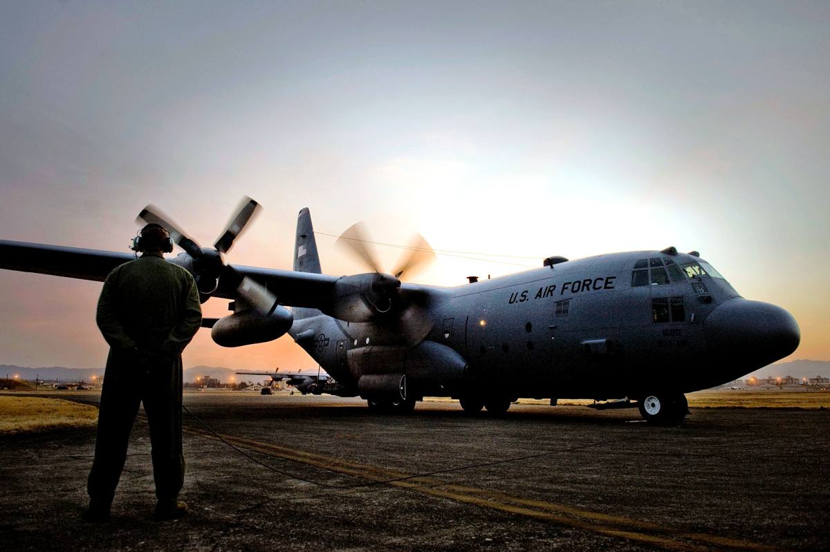 A C-130 aircraft on the flight line at dusk with a crew member standing nearby
